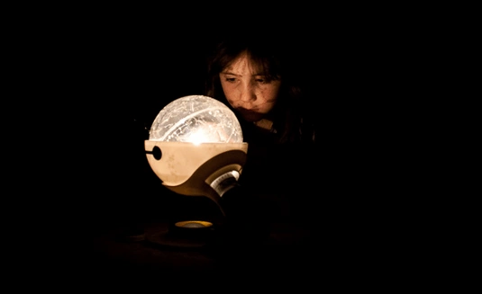 A girl gazes into a lighted globe, showing the solar system.