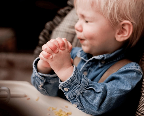 A little boy, hands clasped tightly and eye squinched shut, says his prayers.