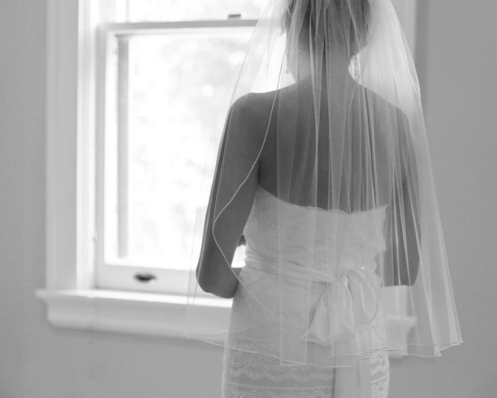 A bride, dressed for her wedding, looks out a window.